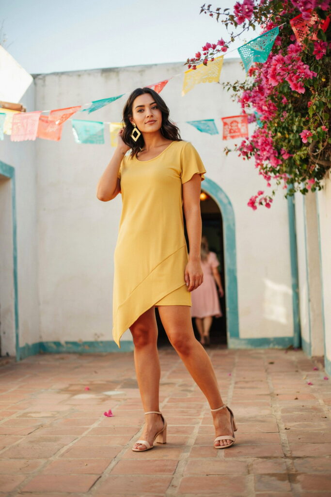 23 Plus Size Cinco de Mayo Outfit Ideas for the Cutest Fiesta Look Ever 17 Plus-size woman wearing an electric yellow asymmetric hem dress with nude heeled sandals and bold geometric earrings, creating a vibrant and flattering Cinco de Mayo outfit for a stylish warm-weather celebration.