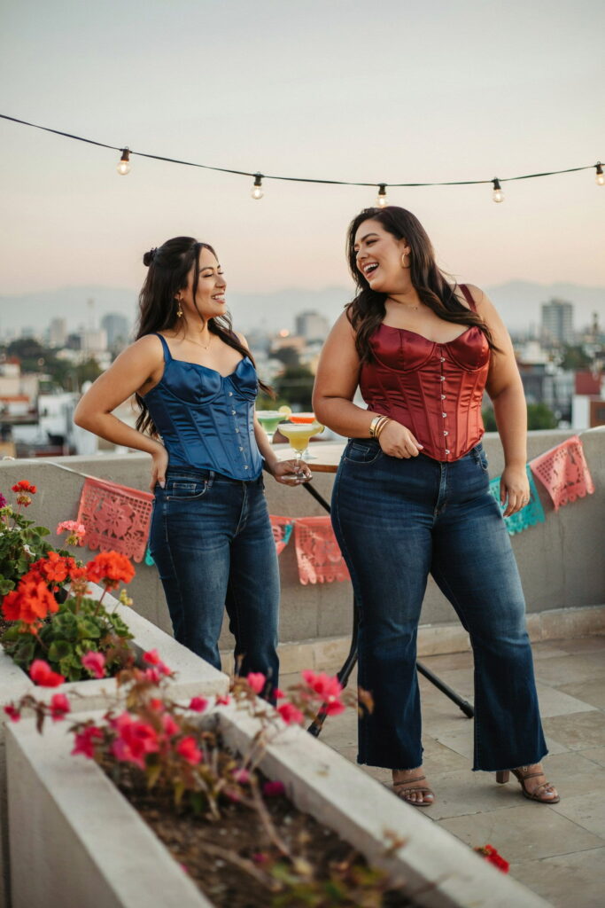 23 Plus Size Cinco de Mayo Outfit Ideas for the Cutest Fiesta Look Ever 24 Woman wearing a deep red corset-style top with high-waisted dark indigo flare jeans and heeled sandals, creating a chic and modern plus-size Cinco de Mayo outfit for a festive celebration.