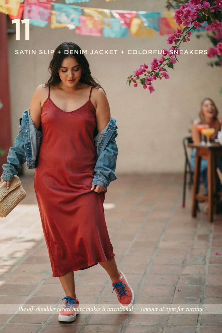 Plus-size woman wearing a deep red satin slip dress layered with an off-the-shoulder light wash denim jacket and colorful chunky sneakers, creating a trendy and comfortable Cinco de Mayo daytime outfit.