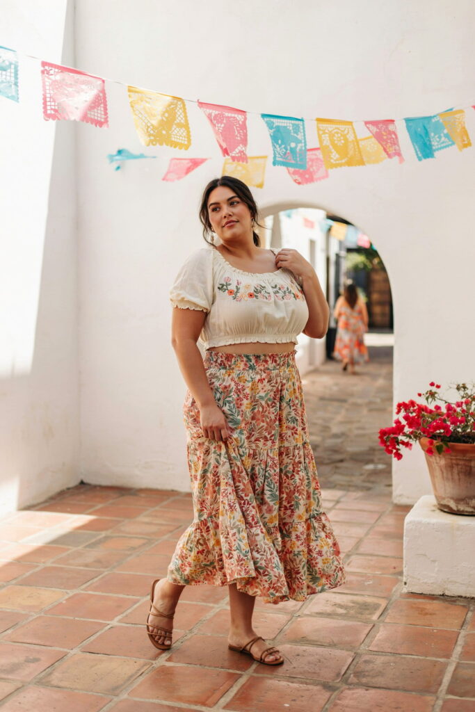 23 Plus Size Cinco de Mayo Outfit Ideas for the Cutest Fiesta Look Ever 10 Plus-size woman wearing a smocked crop top with a high-waisted floral maxi skirt and flat sandals, creating a flattering, feminine Cinco de Mayo outfit perfect for daytime fiestas and evening celebrations.