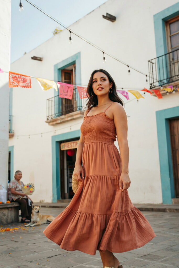 Curvy woman wearing a warm terracotta smocked maxi dress with gold sandals and oversized hoop earrings, perfect for a Cinco de Mayo outdoor fiesta