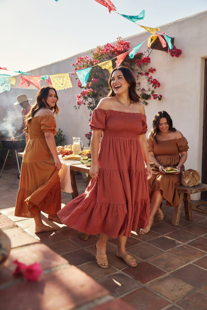 Curvy woman wearing a fiesta red tiered peasant dress with a smocked bodice, woven leather sandals, and a gold necklace for a Cinco de Mayo celebration.