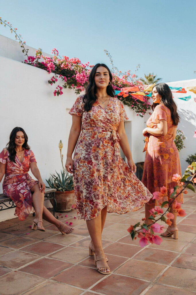 Curvy woman wearing a bold floral wrap midi dress in fuchsia, orange, and deep rose with strappy block-heeled sandals for a stylish Cinco de Mayo outfit